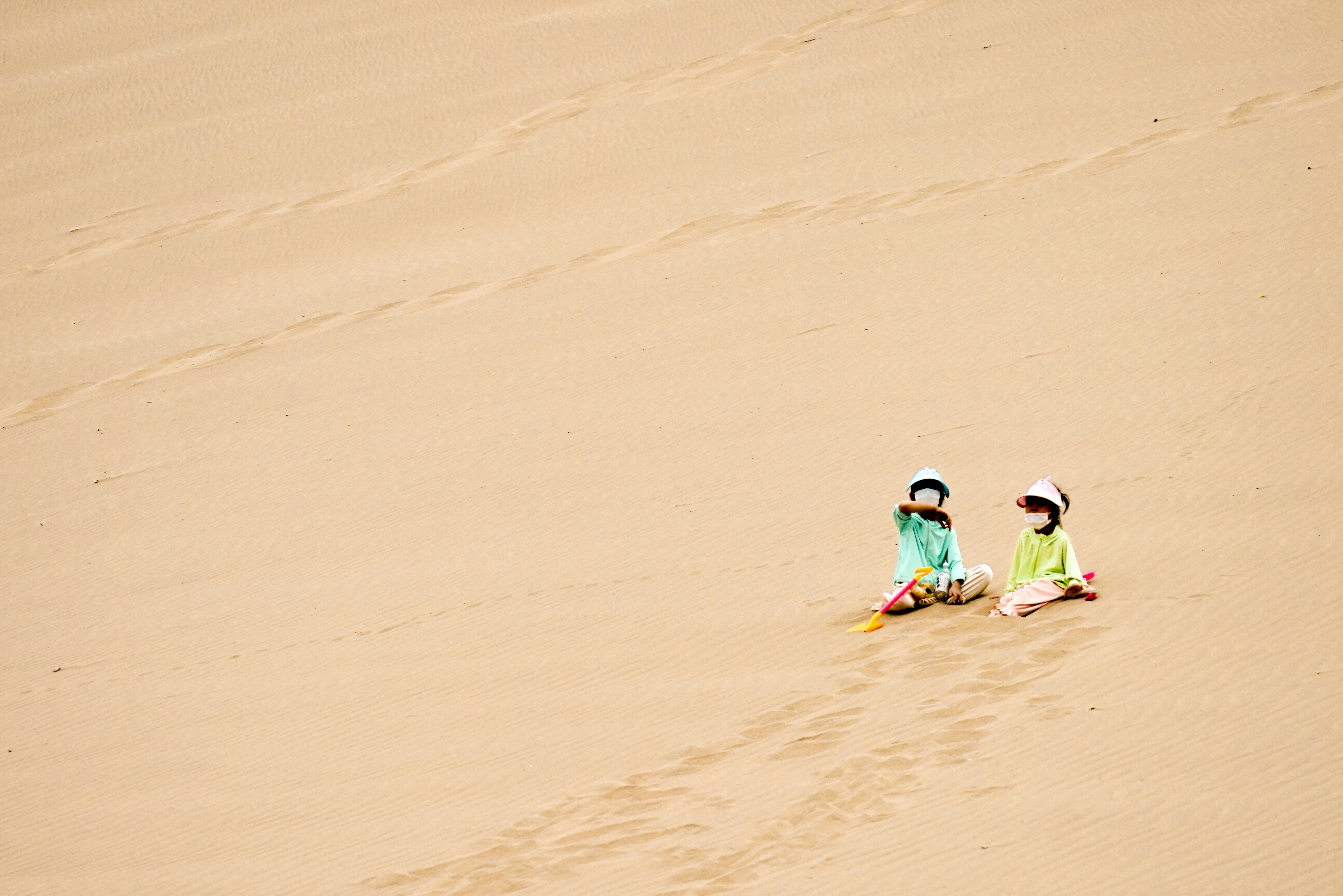 2 children in green and yellow wet suit walking on brown sand during daytime